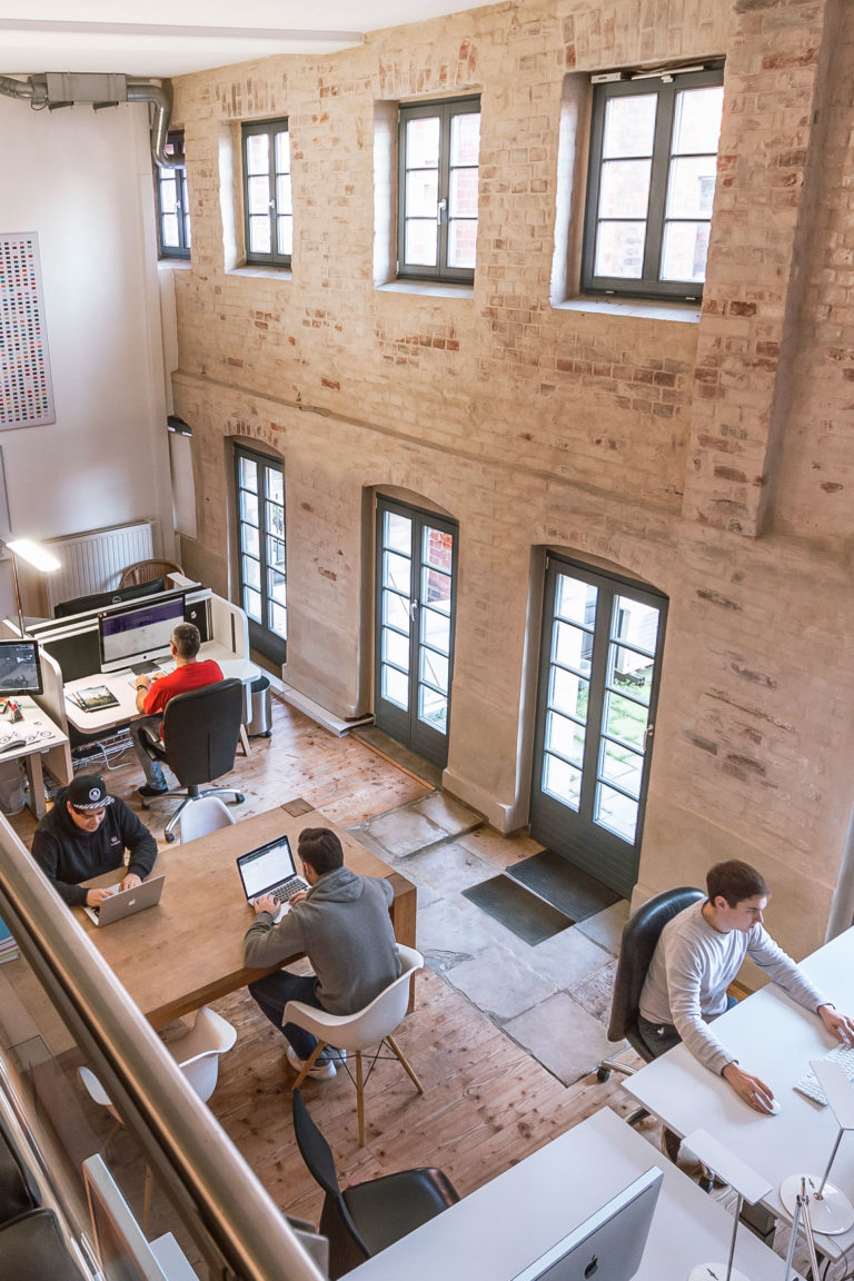 Sudhaus - 4 Personen an Schreibtischen im CoWorkingSpace . Blick von der Galerie aus.